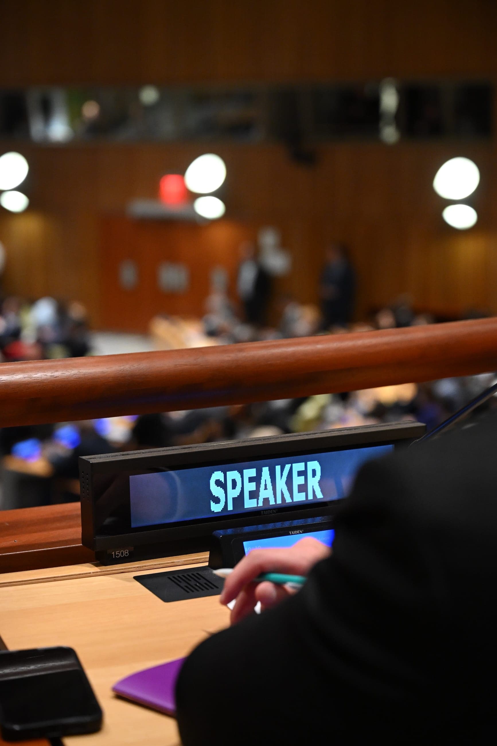 An illuminated Speaker nameplate at a desk in a United Nations conference room.
