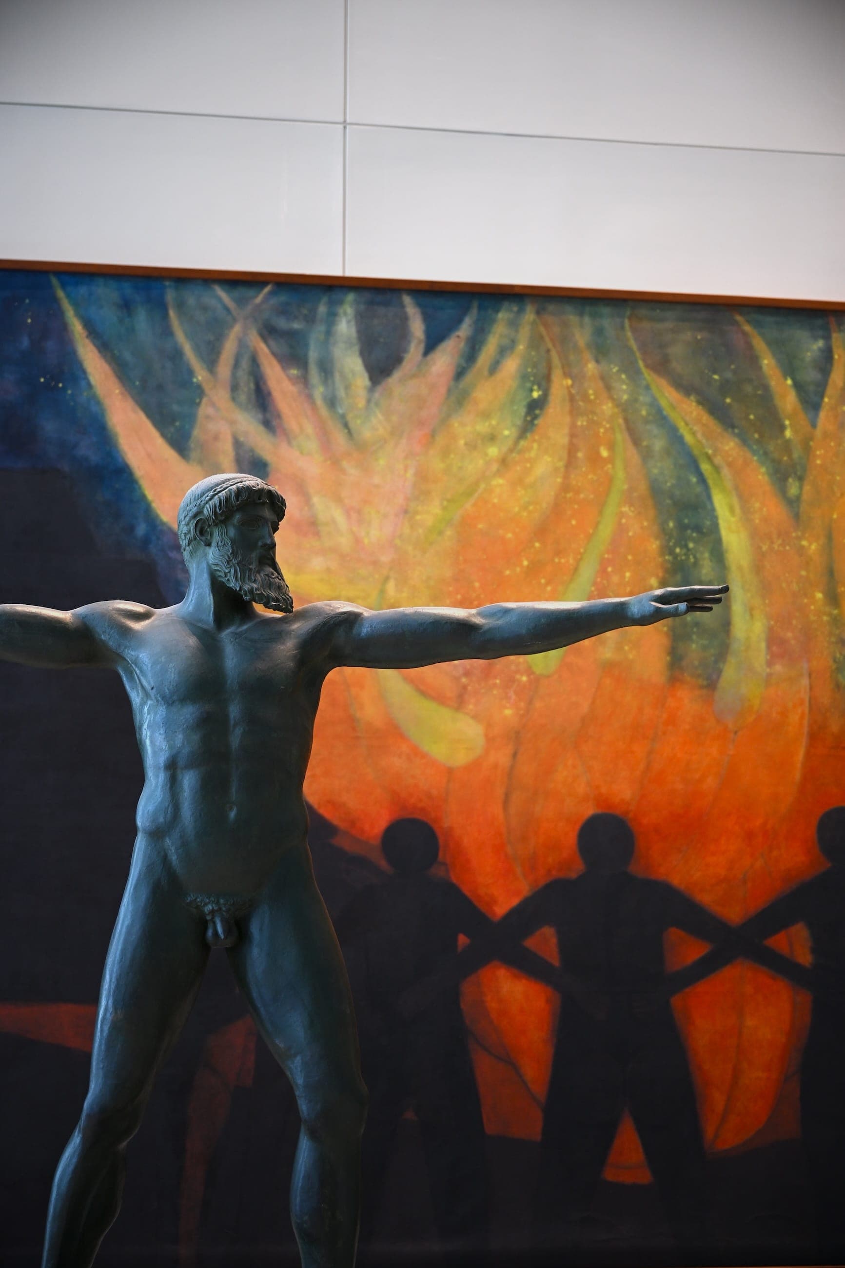 A bronze figure stands with arms outstretched before a mural inside United Nations Headquarters.