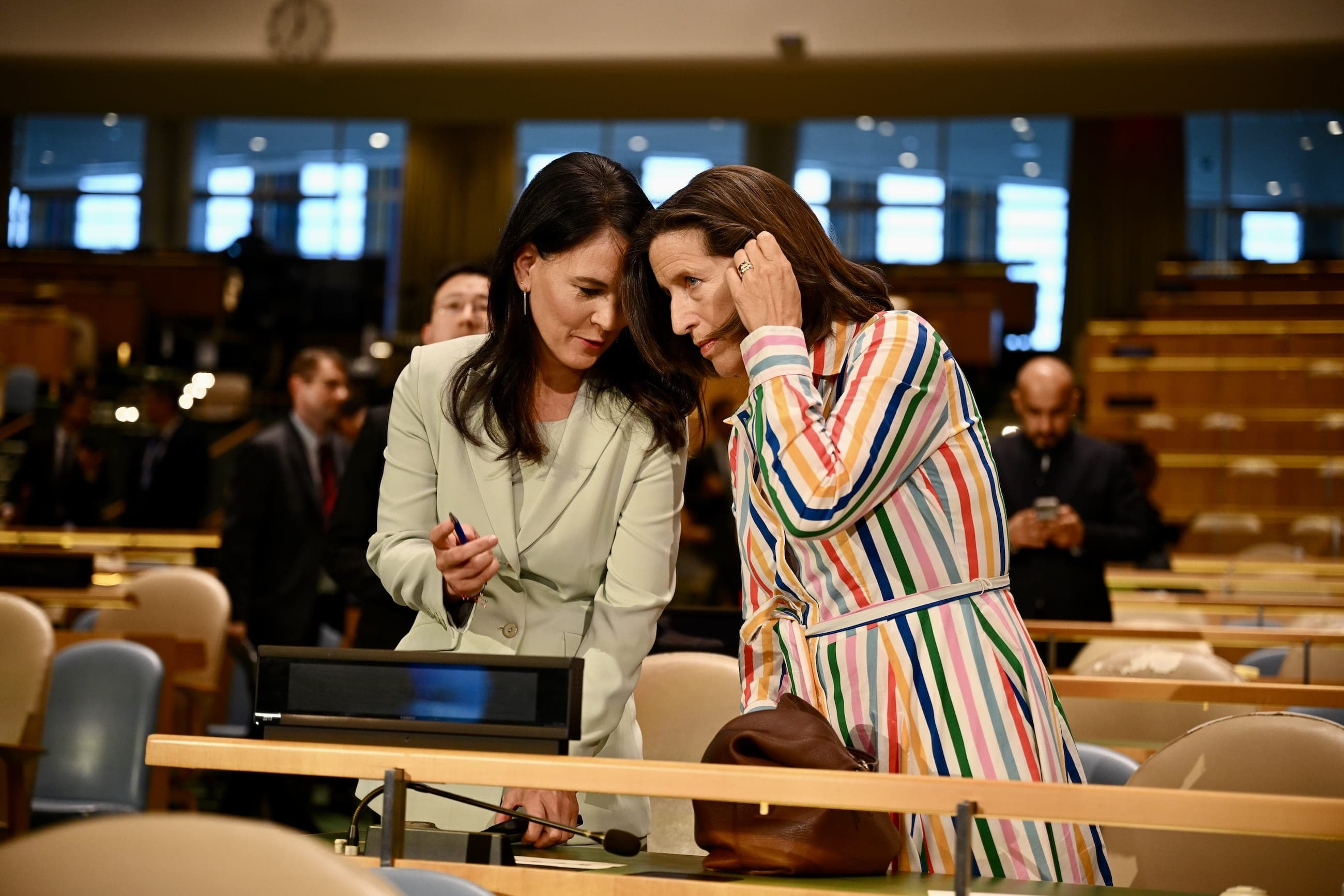 Two women confer at a desk inside the General Assembly Hall.