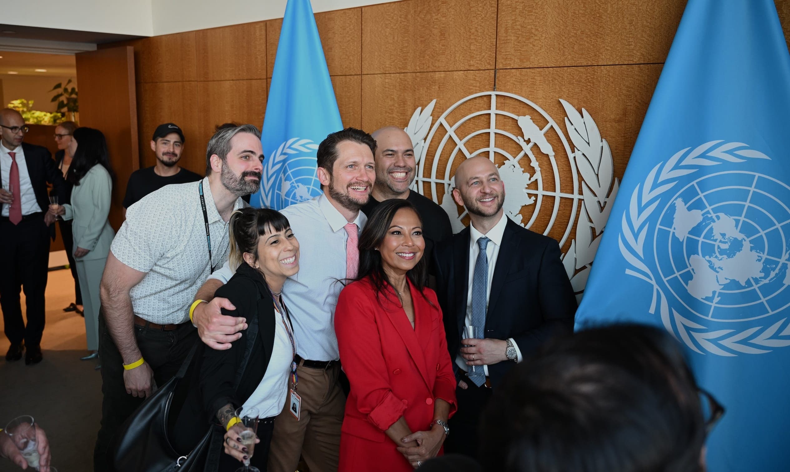 A group poses for a photograph between United Nations flags and the United Nations emblem.