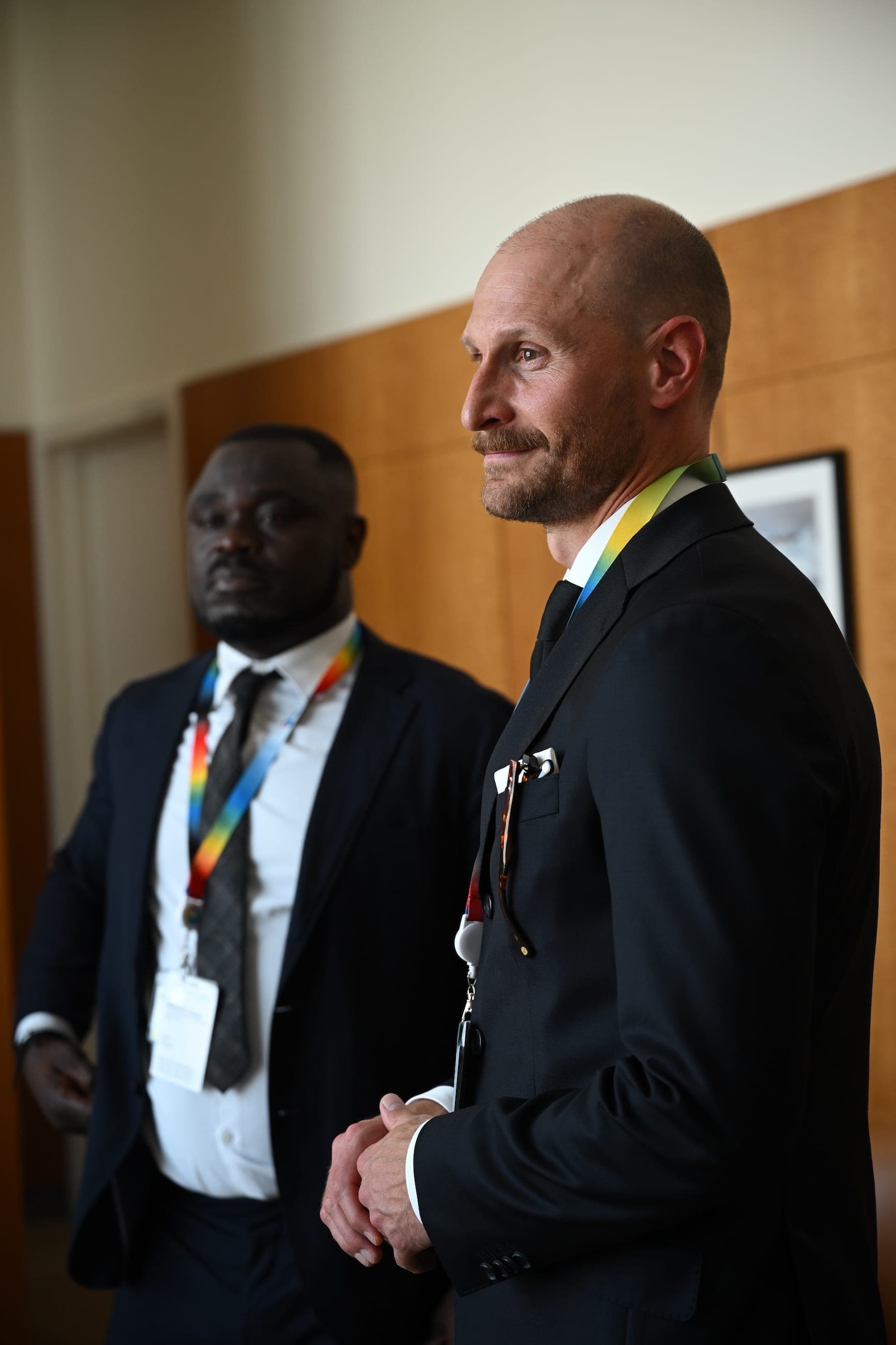 Two conference staff members stand in a meeting room wearing event lanyards.