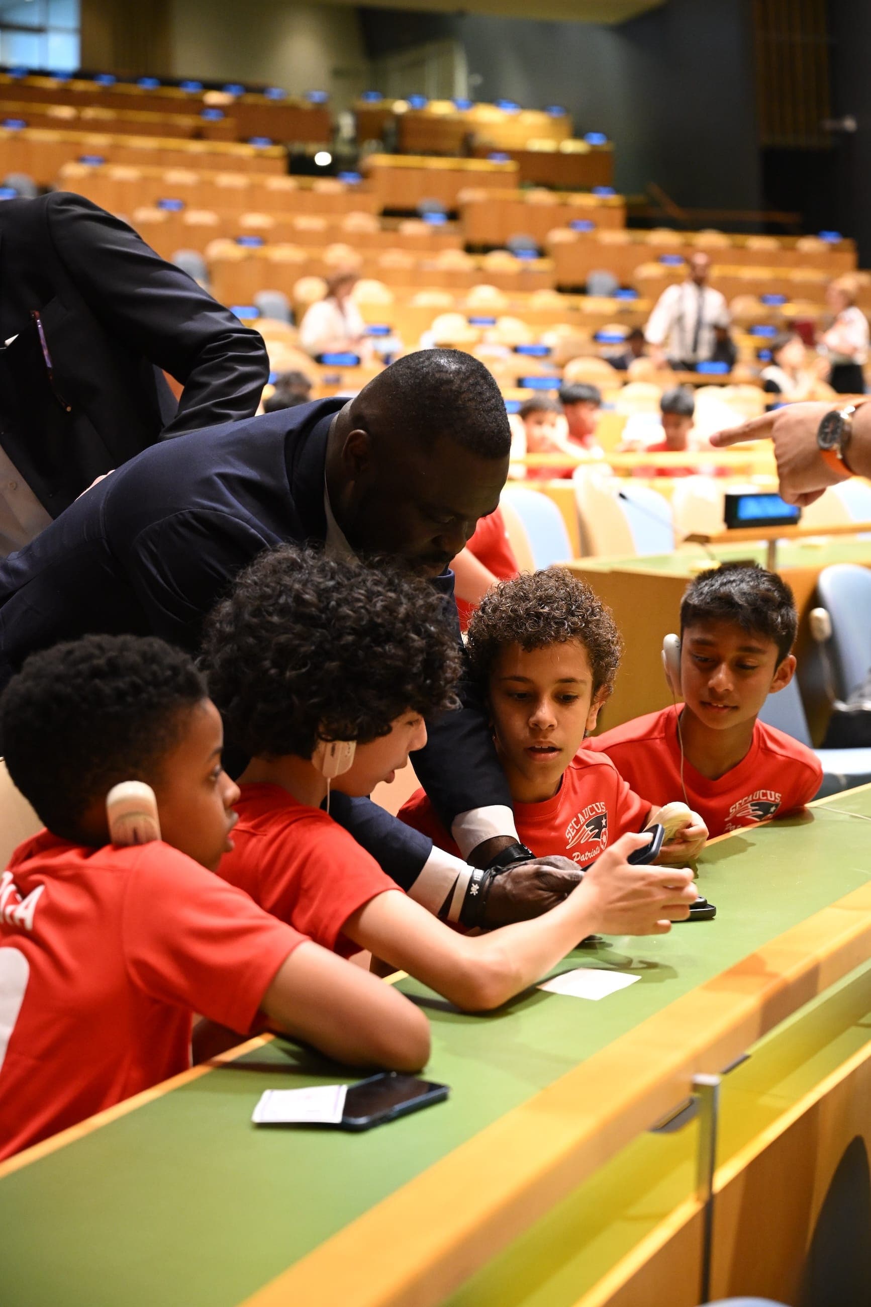A man helps children in red shirts use a phone inside the General Assembly Hall.