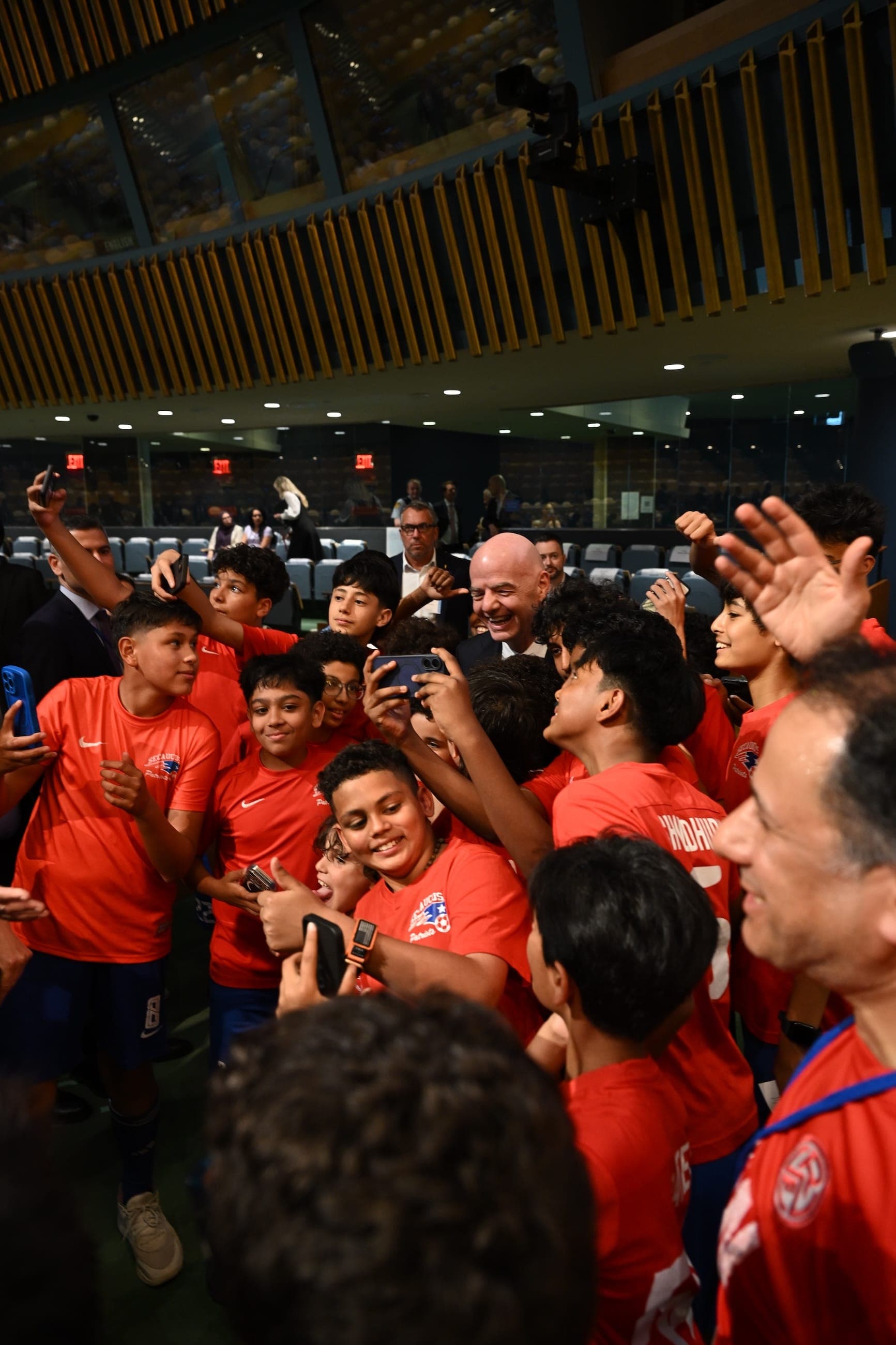 Children in red football shirts gather around an adult for a selfie in the General Assembly Hall.