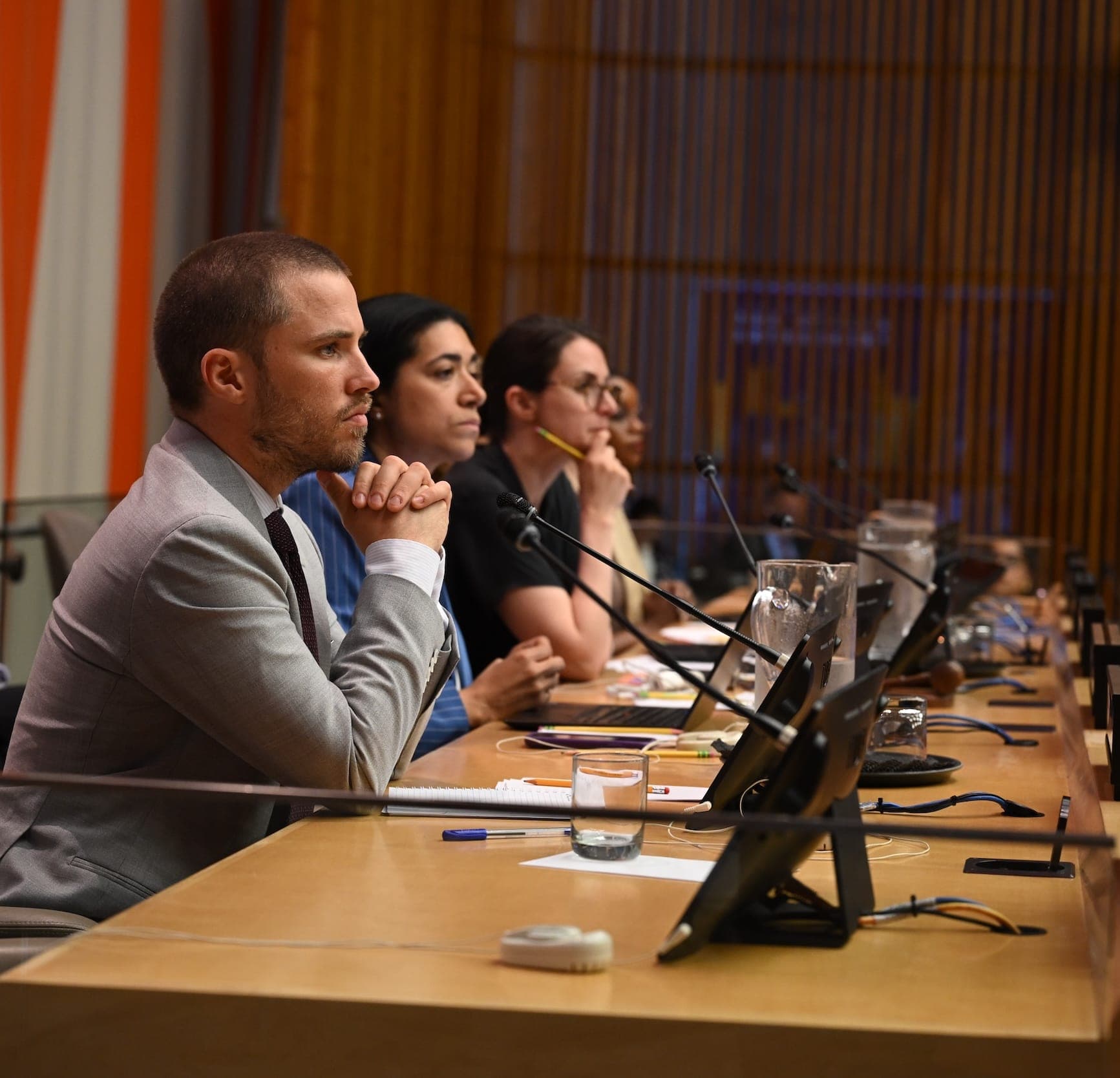 Four delegates listen from a panel table during a meeting.