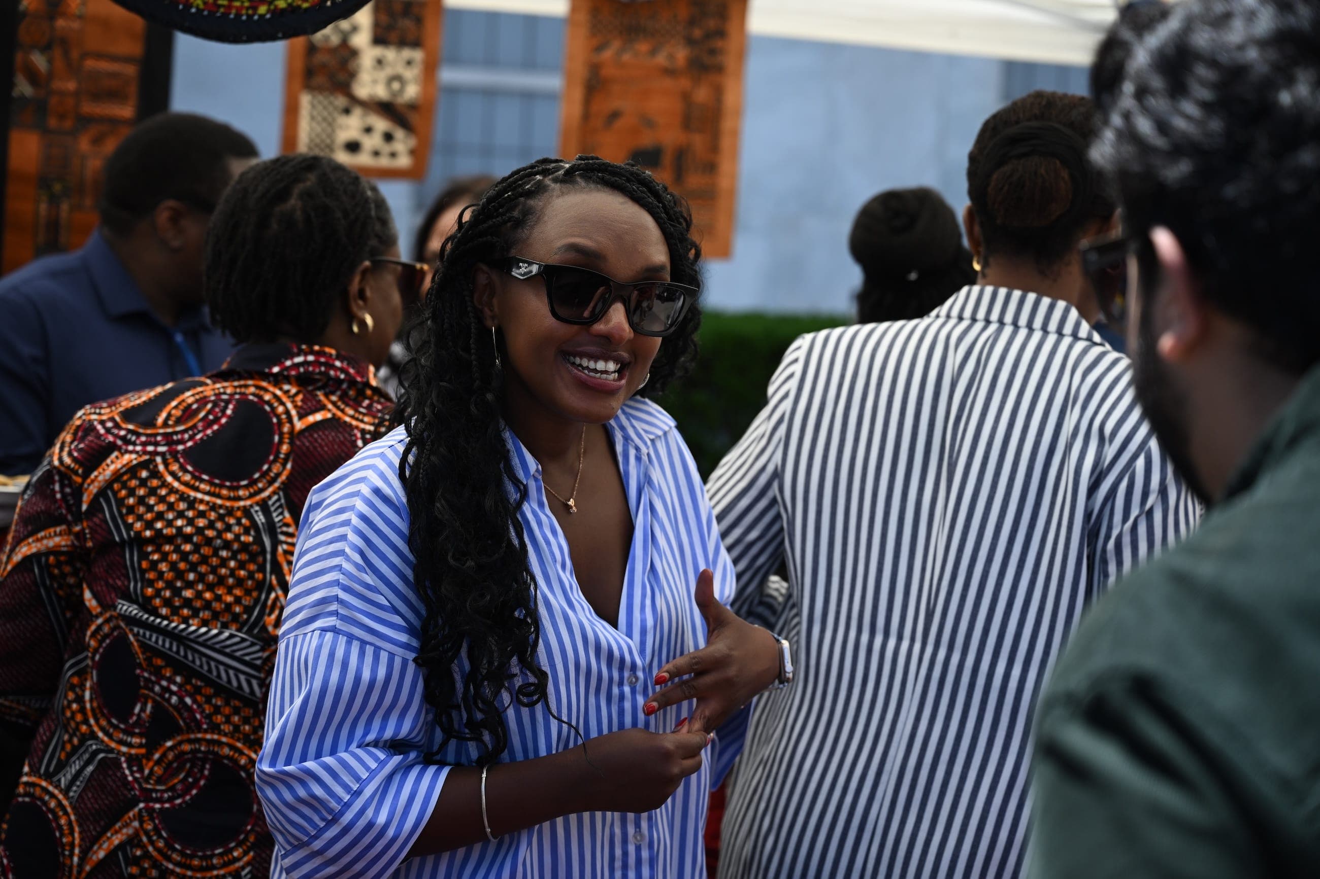 A woman in sunglasses talks with guests at an outdoor cultural event.