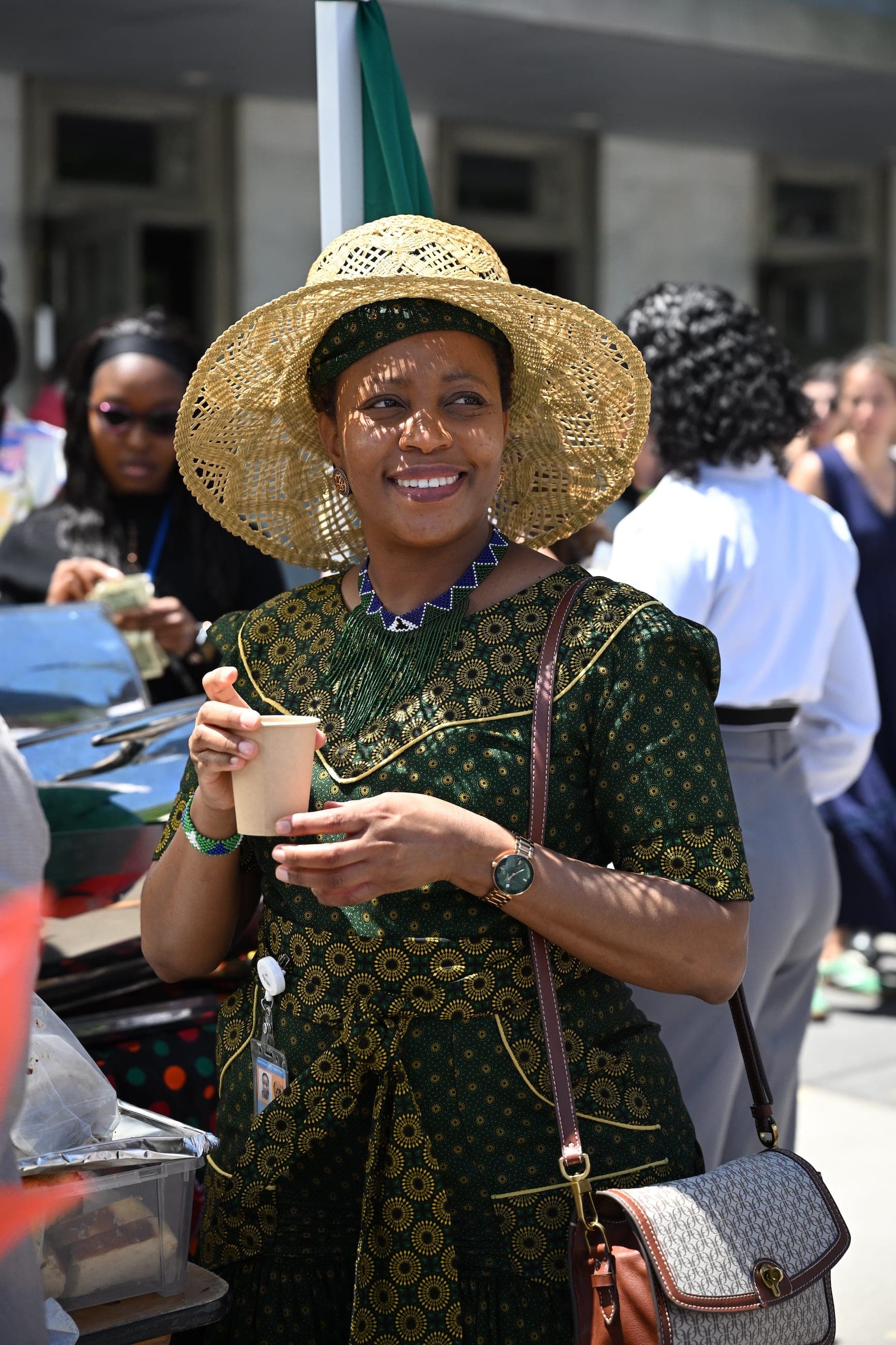 A woman in a wide-brimmed straw hat smiles at an outdoor cultural event.