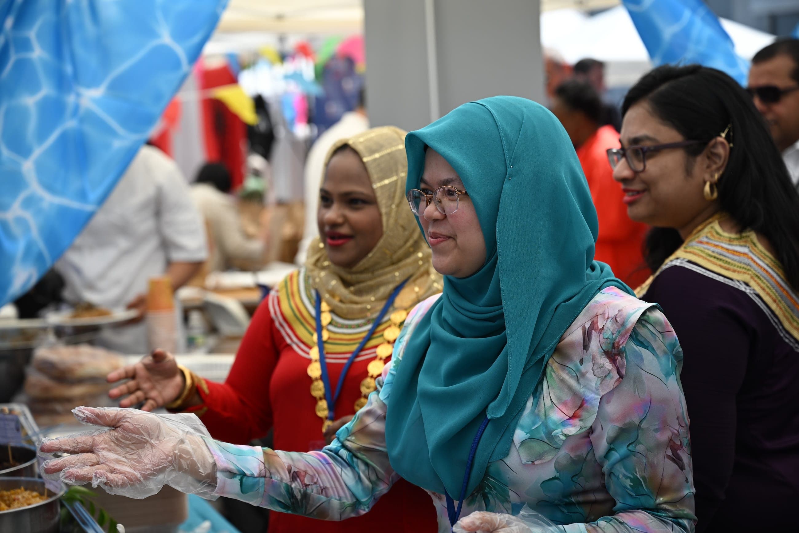 A woman in a teal headscarf serves food at an outdoor cultural event.