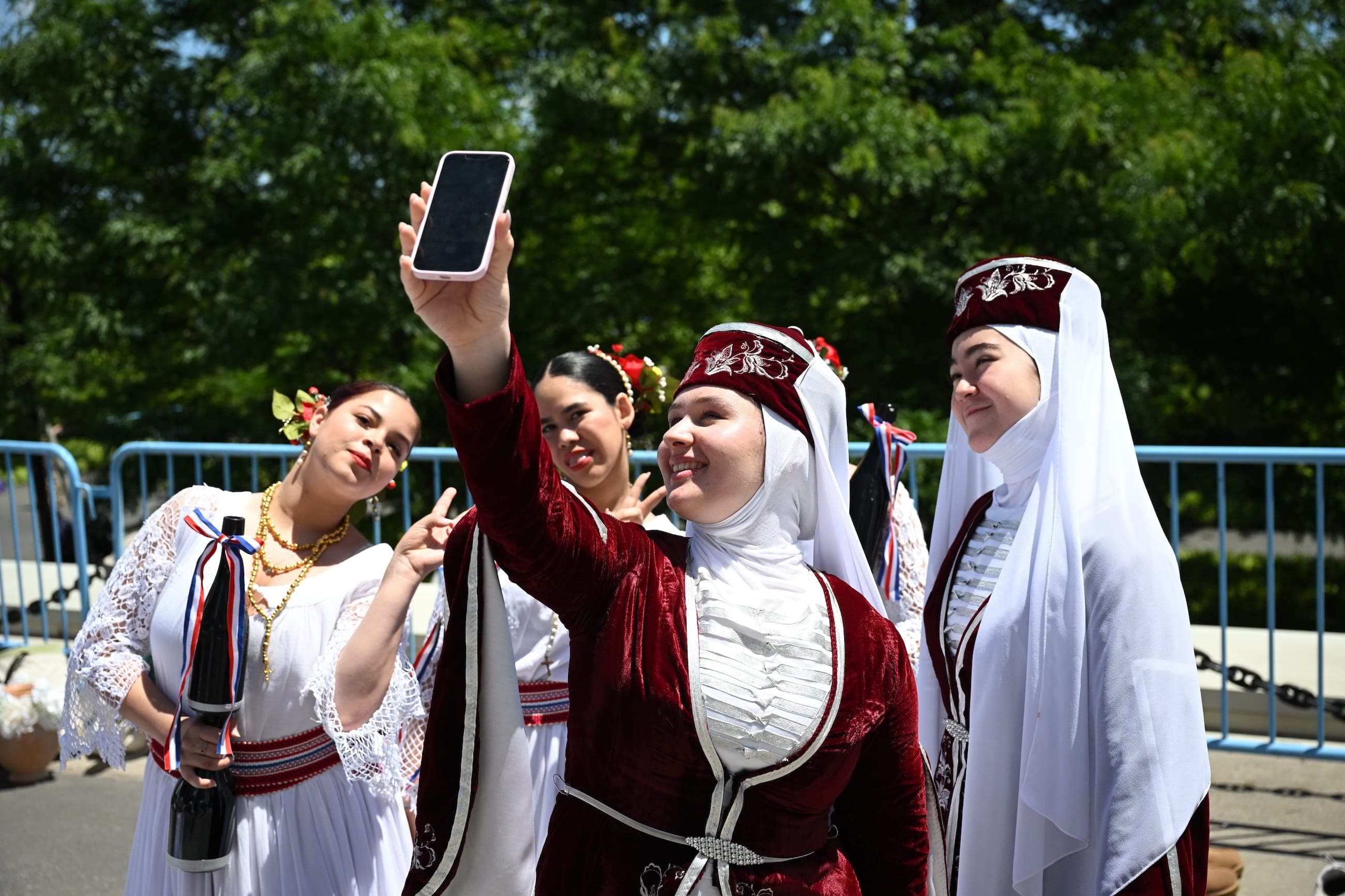 Women in traditional dress take a selfie at an outdoor cultural event.