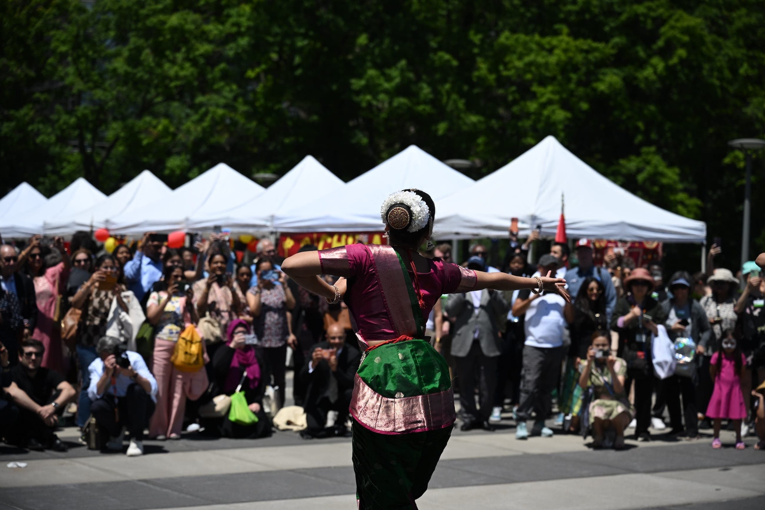 A dancer in traditional dress performs before a crowd at an outdoor cultural event.