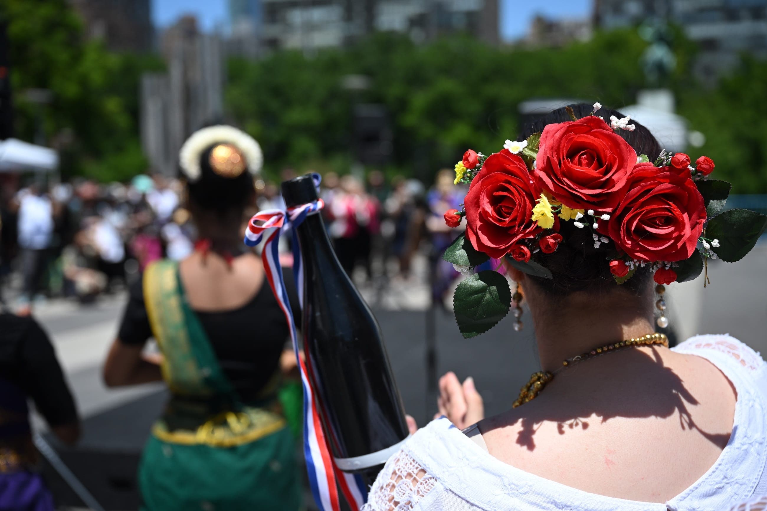A woman wears red roses in her hair at an outdoor cultural event.