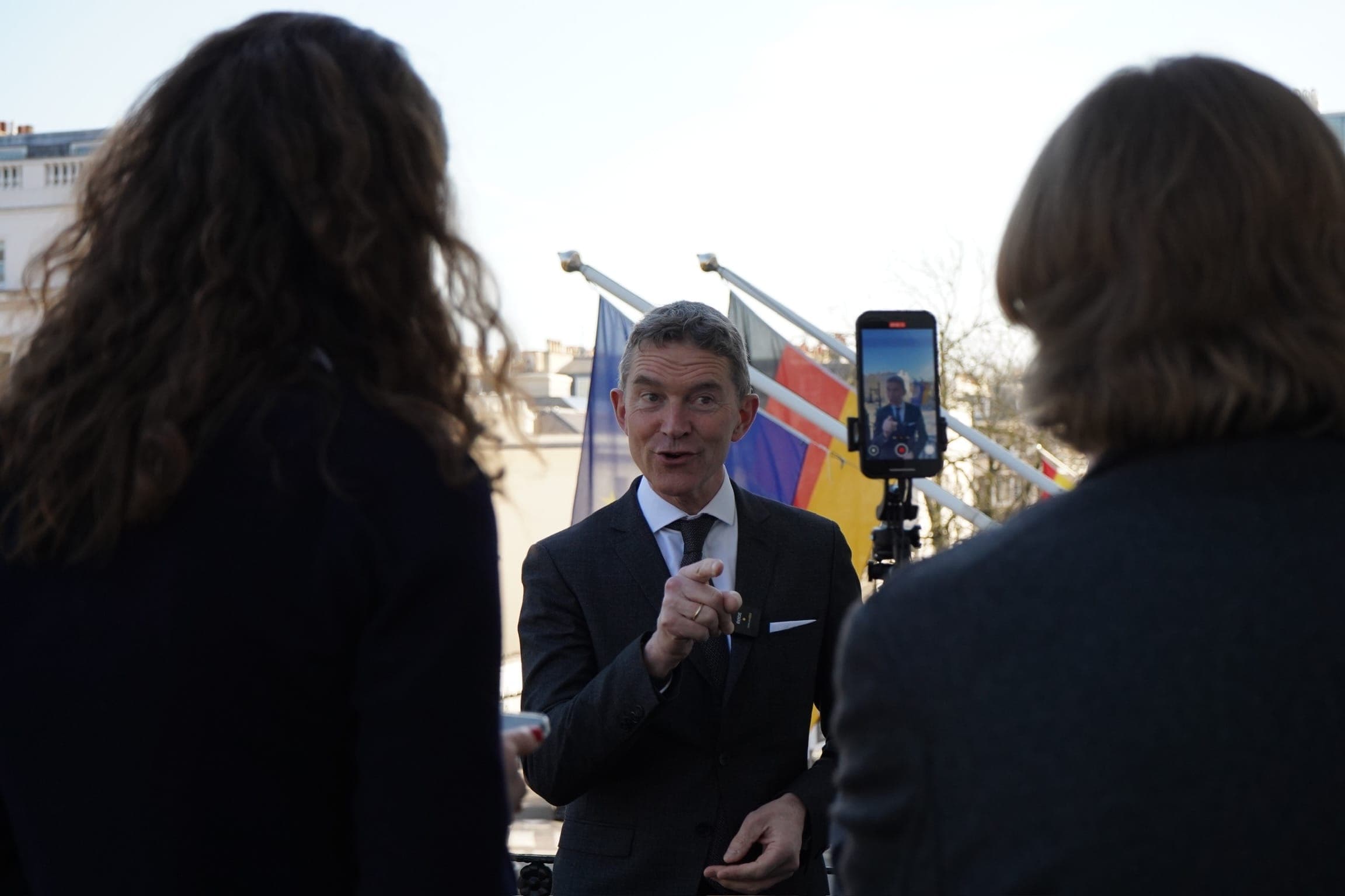 A speaker answers questions outdoors while being recorded on a smartphone