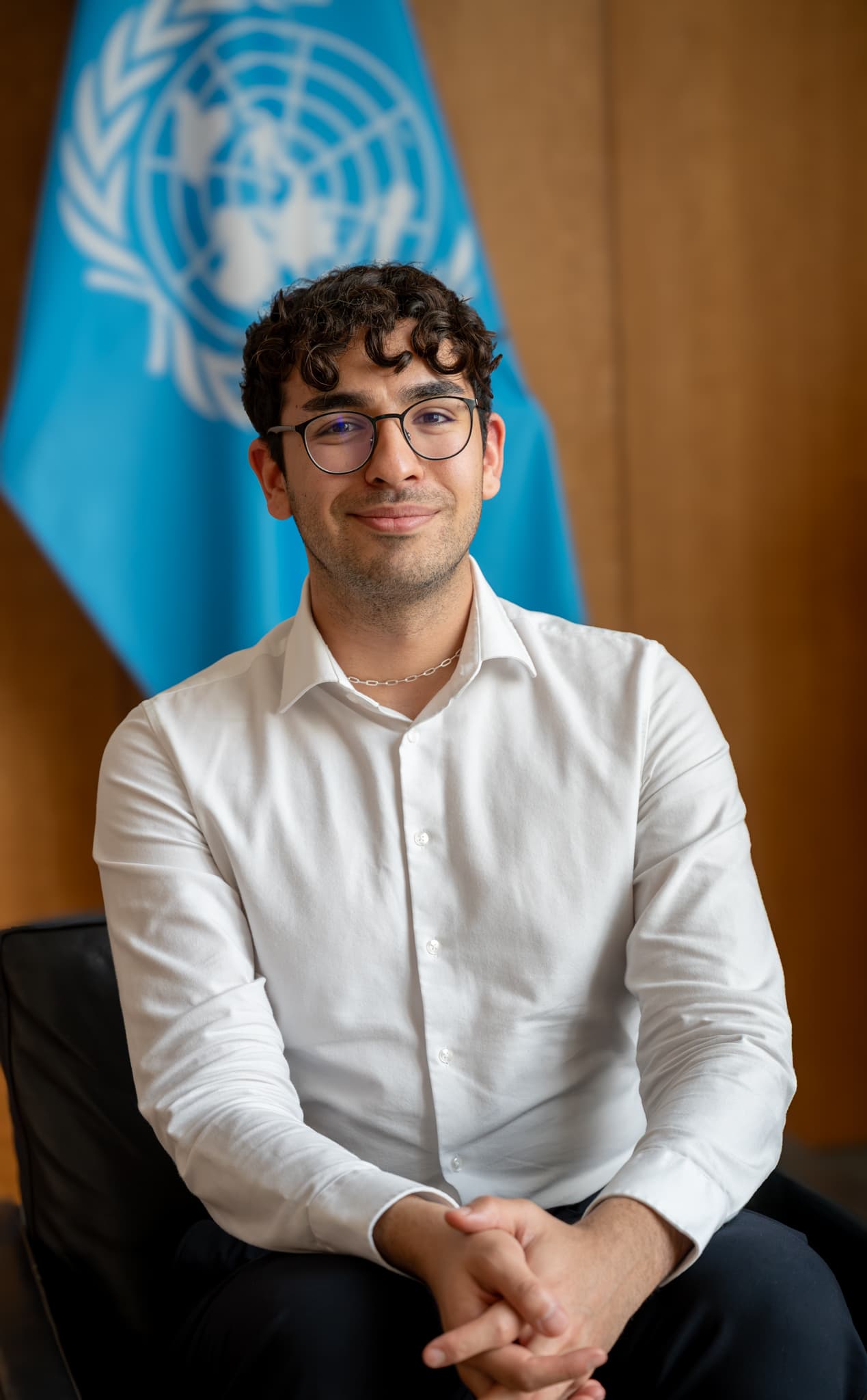 Portrait of Emirhan Dalci seated in front of a United Nations flag