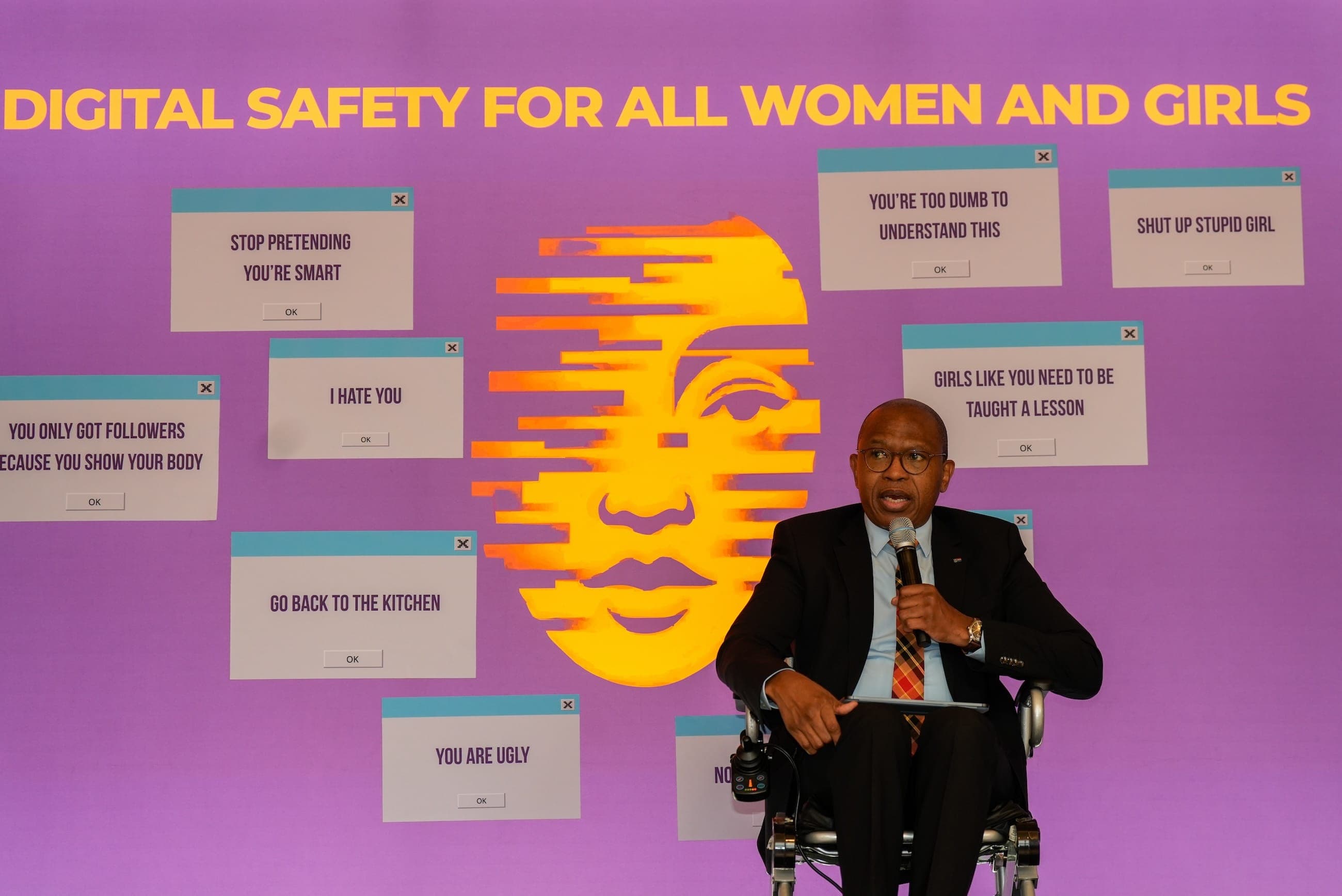 A speaker addresses the event in front of the digital safety installation displaying examples of abusive online messages.